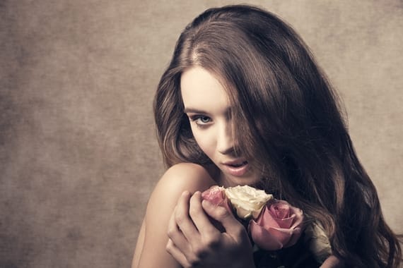 close-up portrait of sensual lady with long hair, taking bouquet of white and pink roses in the hands. Romantic expression and perfect skin, looking in camera
