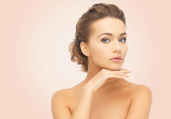 beauty, people and health concept - beautiful young woman touching her face over pink background